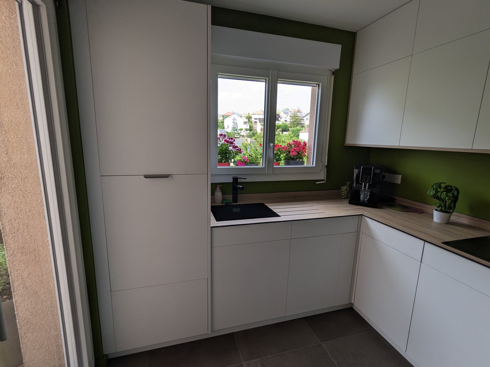 Cuisine compacte en angle avec façades blanches, plan de travail ton bois et murs verts